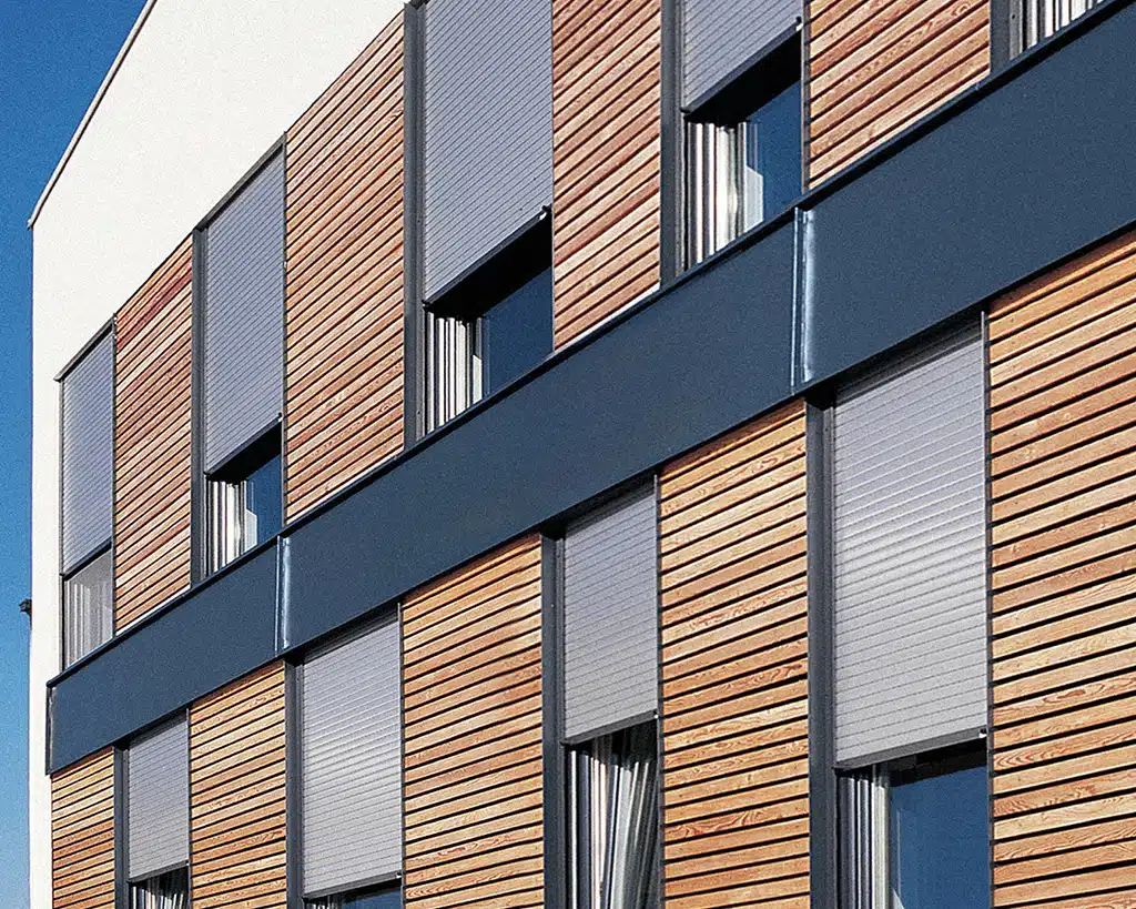 Moderne Hausfassade mit Holzverkleidung und geschlossenen grauen Rollläden von KATZBECK für optimalen Sonnenschutz und Schalldämmung.