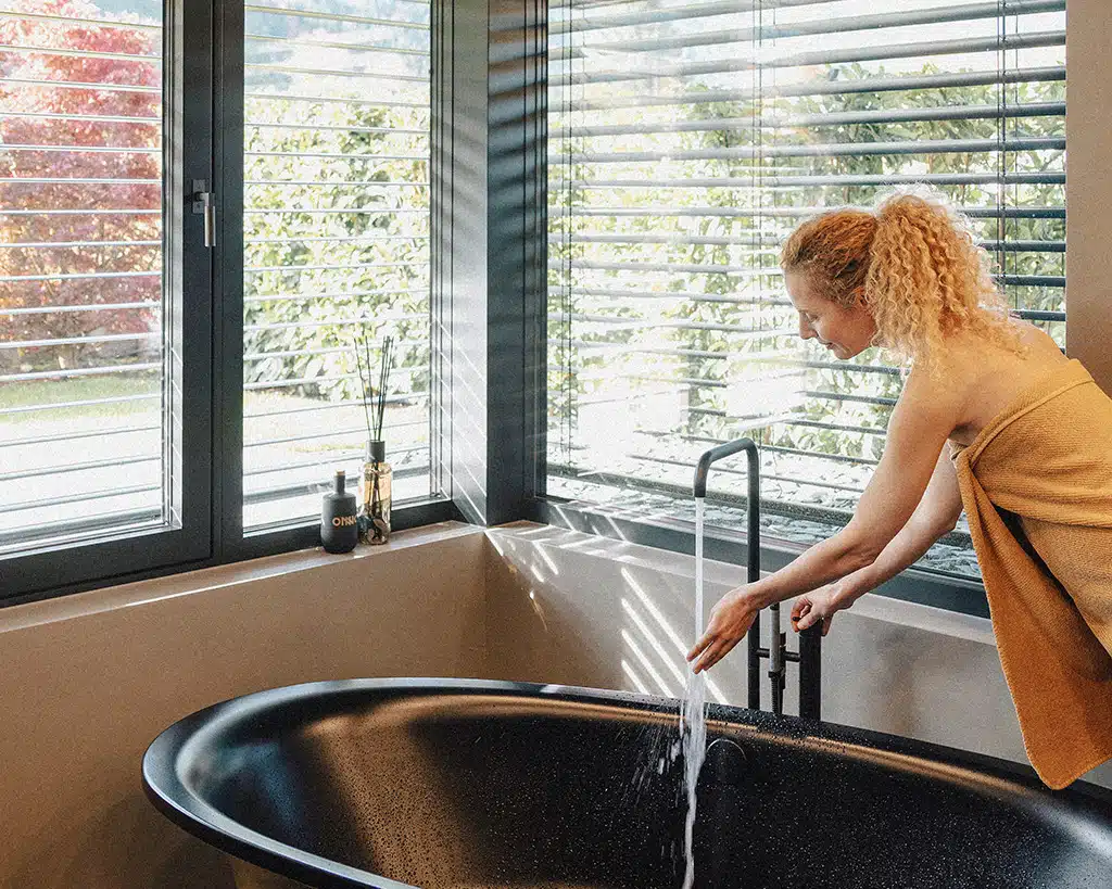 Modernes Badezimmer mit großen Eckfenstern und KATZBECK Raffstoren, die für optimal reguliertes Tageslicht und Hitzeschutz an der Badewanne sorgen.