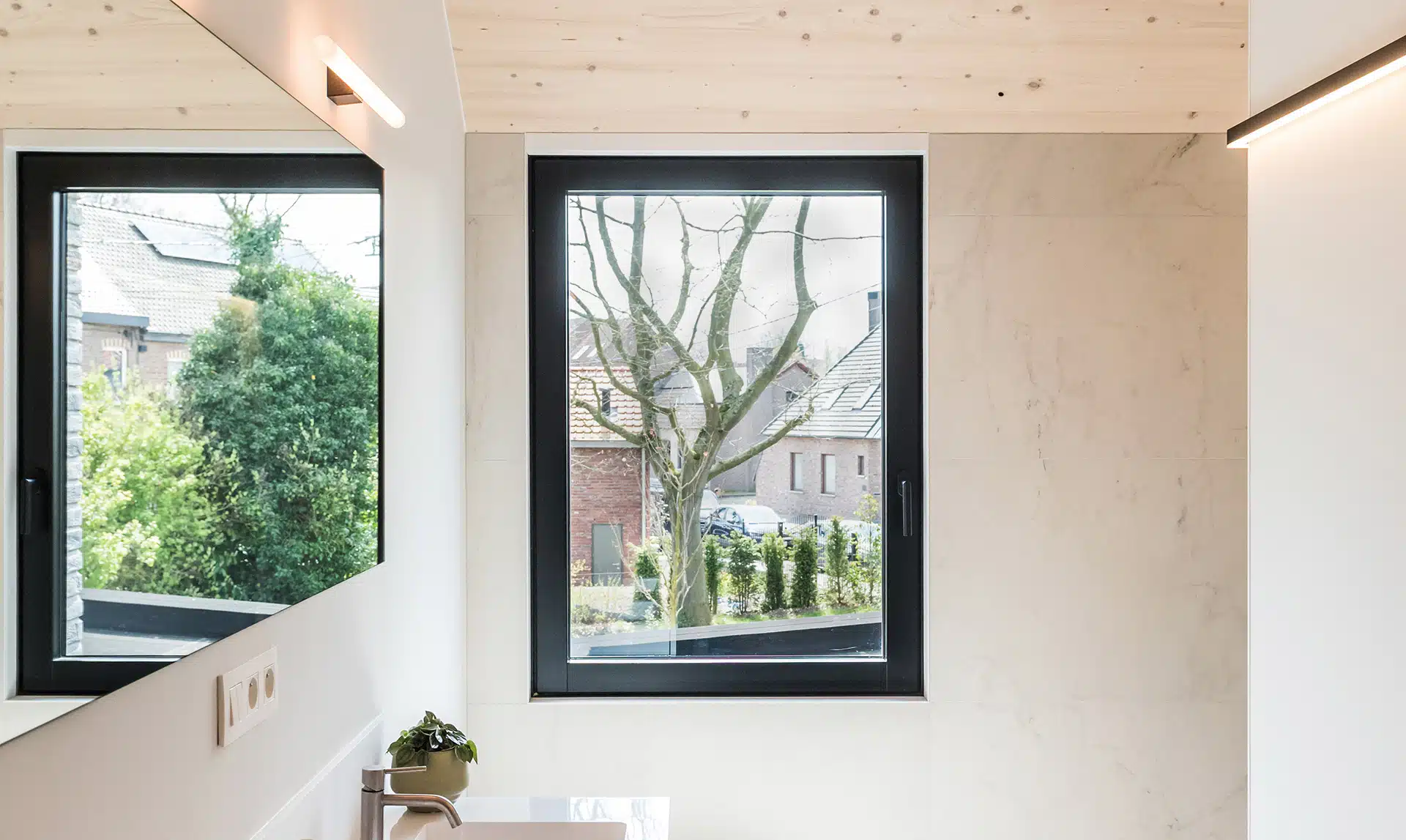 Modernes Badezimmer mit großen, dunklen KATZBECK Holz-Alu-Fensterrahmen, die einen klaren Kontrast zu den weißen Marmorfliesen und der hellen Holzdecke bilden.